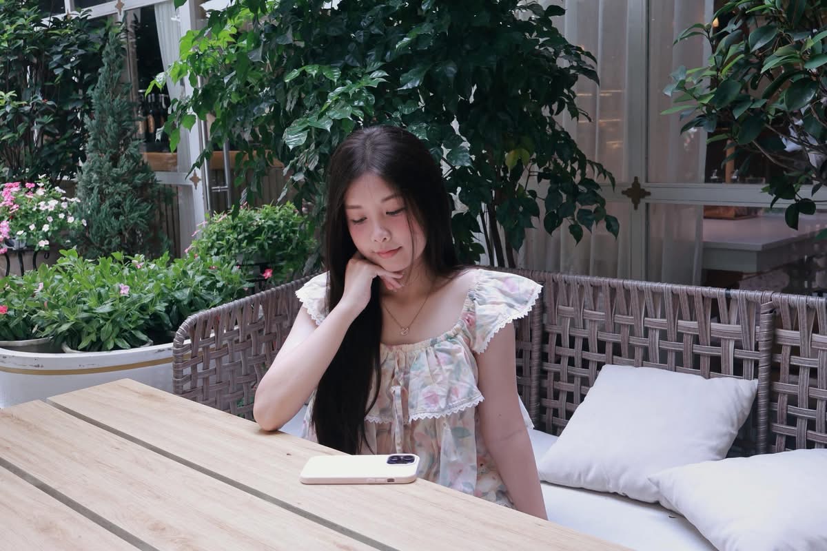 A girl in a white dress rests her hand on her cheek, relaxing in an outdoor café setting.